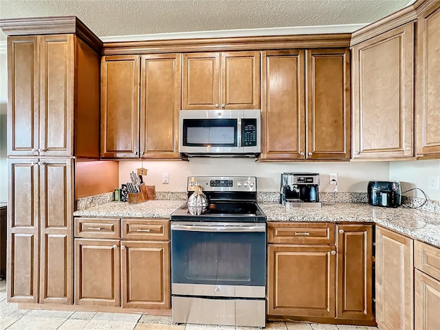 kitchen with light stone countertops, a textured ceiling, light tile patterned floors, and appliances with stainless steel finishes