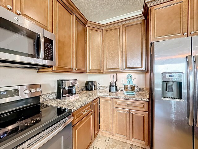 kitchen featuring light stone countertops, a textured ceiling, light tile patterned floors, and appliances with stainless steel finishes