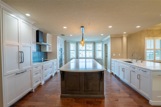 kitchen with decorative light fixtures, sink, wall chimney range hood, and white cabinetry