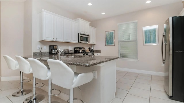 kitchen featuring white cabinetry, appliances with stainless steel finishes, dark stone counters, and a breakfast bar