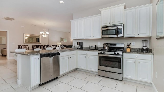 kitchen featuring stainless steel appliances, white cabinets, kitchen peninsula, a notable chandelier, and dark stone countertops