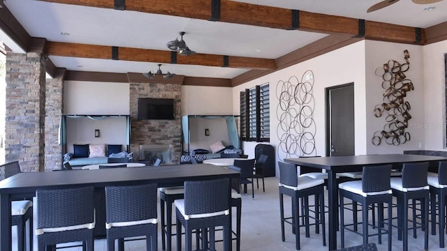 kitchen with a stone fireplace, ceiling fan, and beam ceiling