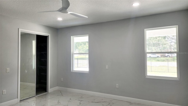 unfurnished bedroom with a textured ceiling, a walk in closet, a closet, and ceiling fan