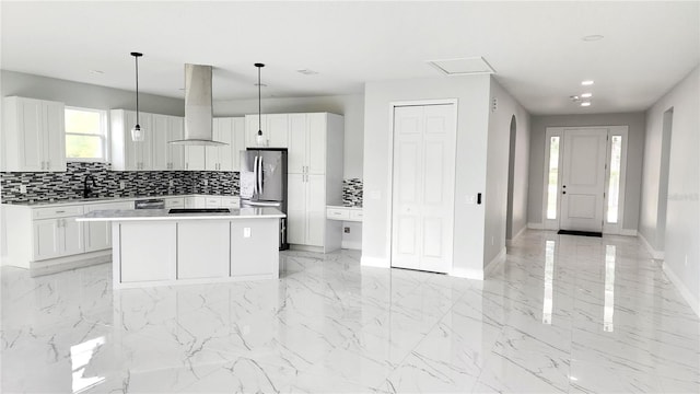 kitchen featuring decorative light fixtures, a center island, wall chimney range hood, and white cabinetry