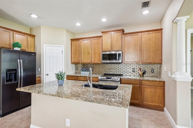 kitchen with ornate columns, sink, an island with sink, and appliances with stainless steel finishes