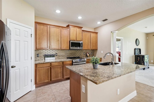 kitchen with sink, light stone counters, a kitchen island with sink, light tile patterned floors, and appliances with stainless steel finishes