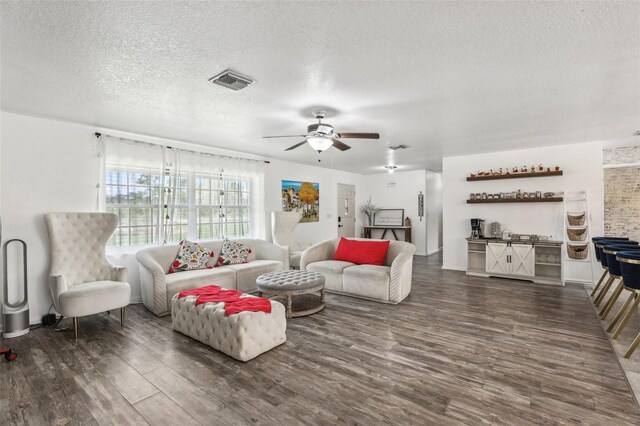 living room featuring dark wood-type flooring, ceiling fan, and a textured ceiling