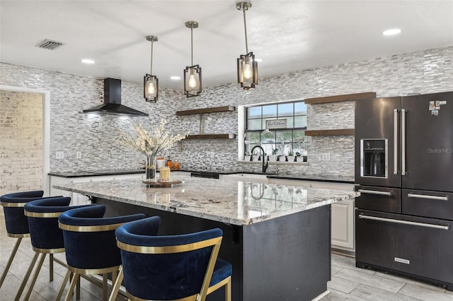 kitchen featuring a kitchen breakfast bar, light stone countertops, a center island, wall chimney range hood, and high end fridge