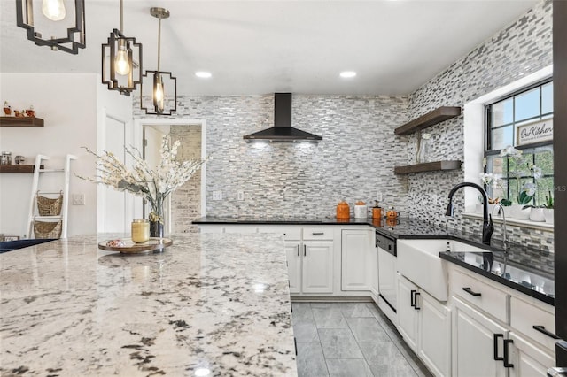 kitchen featuring dark stone counters, white cabinets, dishwasher, wall chimney range hood, and backsplash