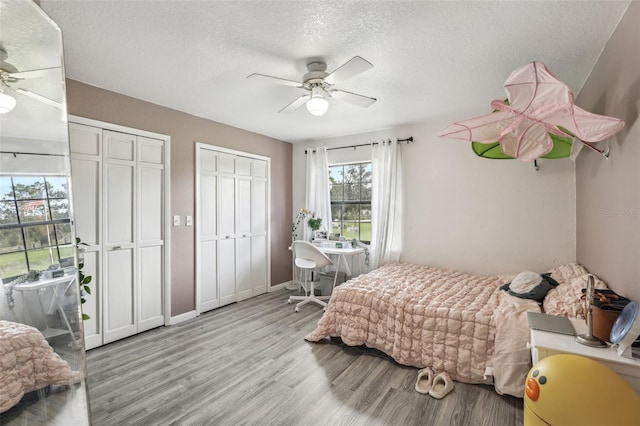 bedroom featuring a textured ceiling, light wood-type flooring, multiple closets, and ceiling fan