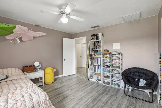 bedroom with a textured ceiling, wood-type flooring, and ceiling fan