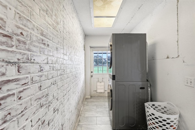 bathroom with stacked washer and dryer and brick wall