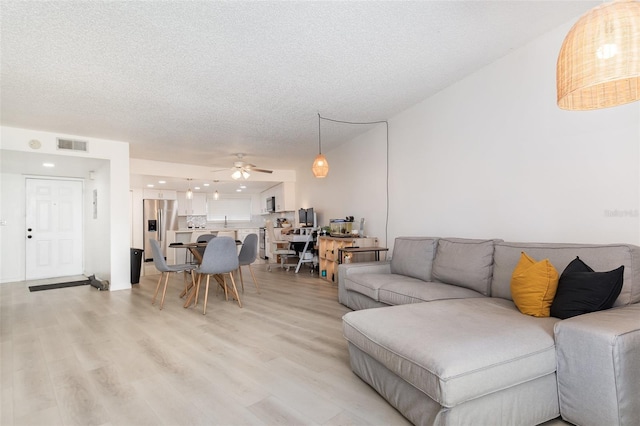 living room featuring ceiling fan, light hardwood / wood-style floors, and a textured ceiling