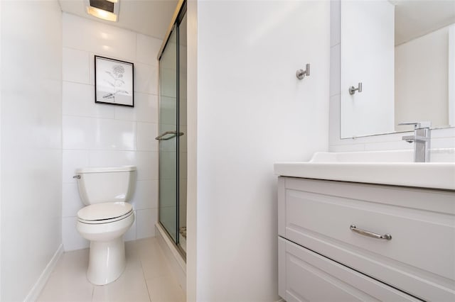 bathroom with tile patterned floors, vanity, a shower with door, tile walls, and toilet