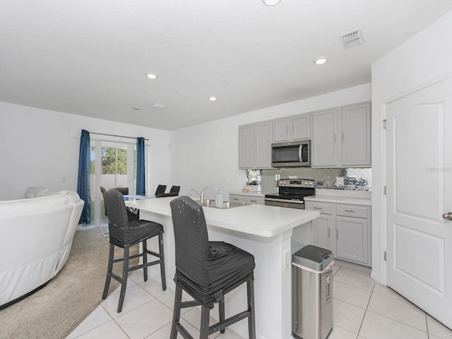 kitchen with a breakfast bar area, gray cabinets, stainless steel appliances, an island with sink, and light tile patterned flooring