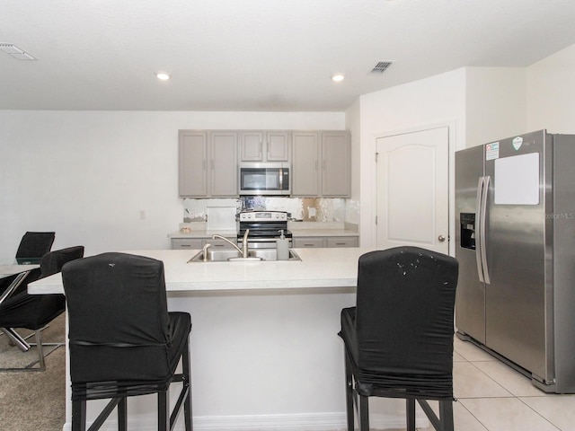 kitchen featuring stainless steel appliances, gray cabinets, light tile patterned floors, and a breakfast bar