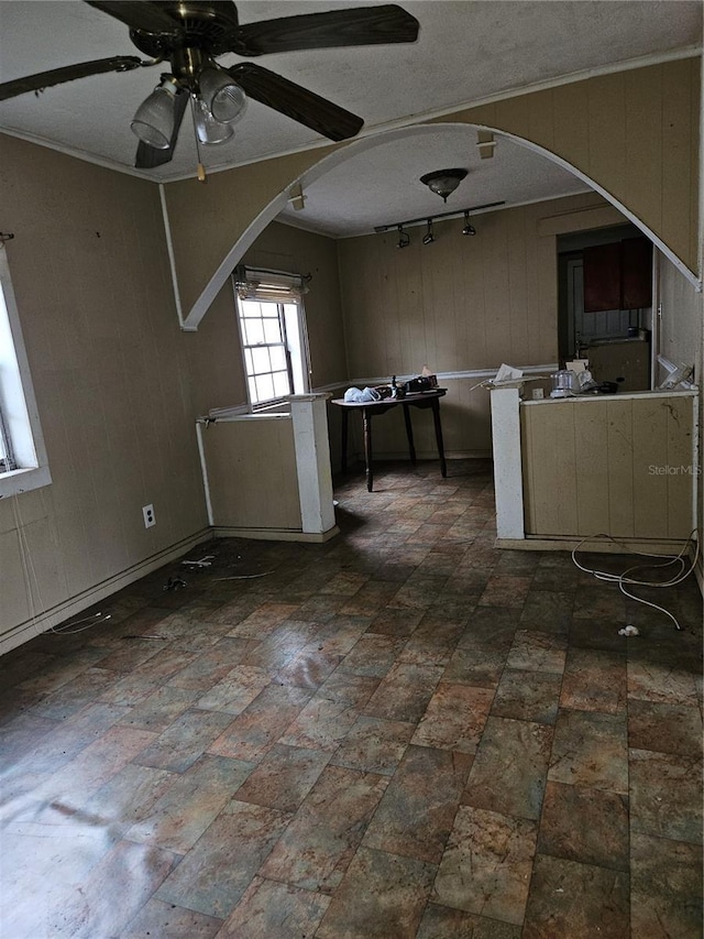 interior space featuring a ceiling fan, arched walkways, wooden walls, and a textured ceiling