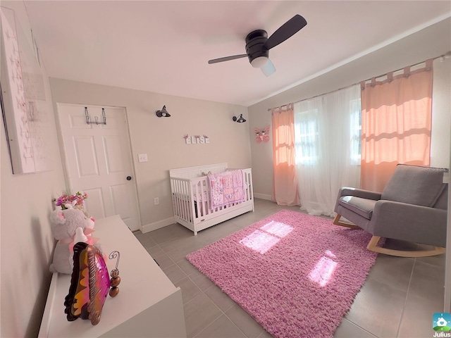 tiled bedroom featuring a nursery area and ceiling fan