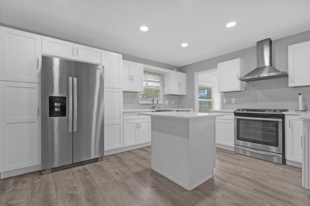 kitchen with white cabinets, appliances with stainless steel finishes, light hardwood / wood-style floors, and wall chimney exhaust hood