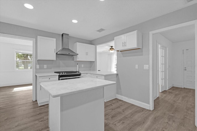 kitchen with wall chimney exhaust hood, gas range, white cabinetry, light hardwood / wood-style floors, and a kitchen island