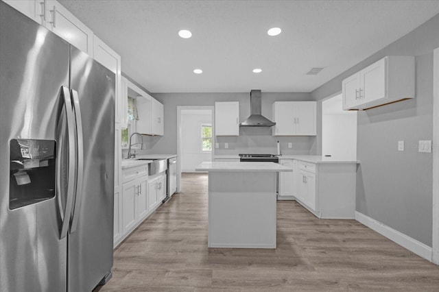 kitchen featuring wall chimney exhaust hood, stainless steel appliances, a center island, light hardwood / wood-style floors, and white cabinetry