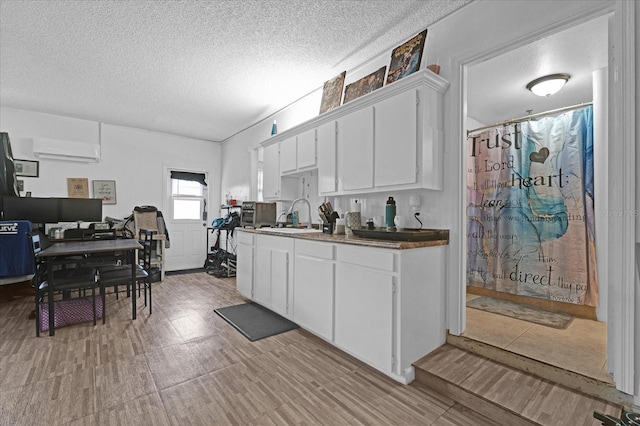 kitchen with a wall mounted air conditioner, white cabinetry, and a textured ceiling