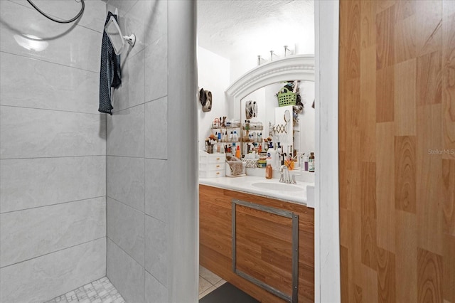 bathroom with tile patterned flooring, vanity, a tile shower, and a textured ceiling