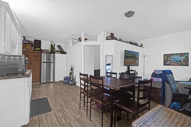 dining area with ceiling fan, wood-type flooring, and a textured ceiling