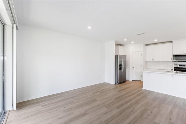 kitchen featuring a kitchen breakfast bar, backsplash, stainless steel appliances, light hardwood / wood-style flooring, and white cabinetry