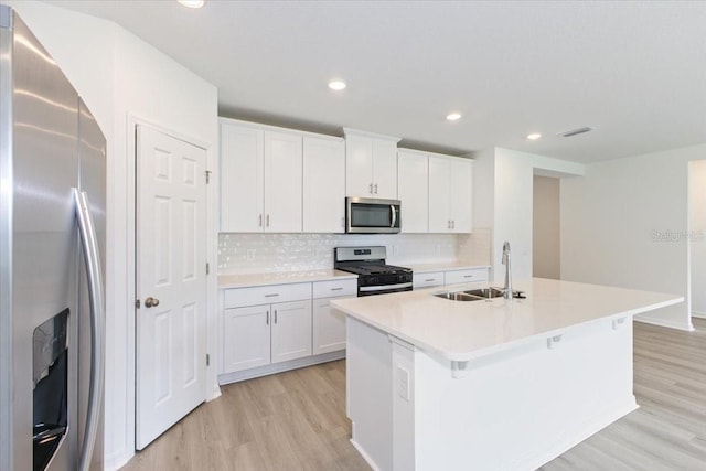 kitchen featuring appliances with stainless steel finishes, sink, light hardwood / wood-style flooring, white cabinets, and an island with sink