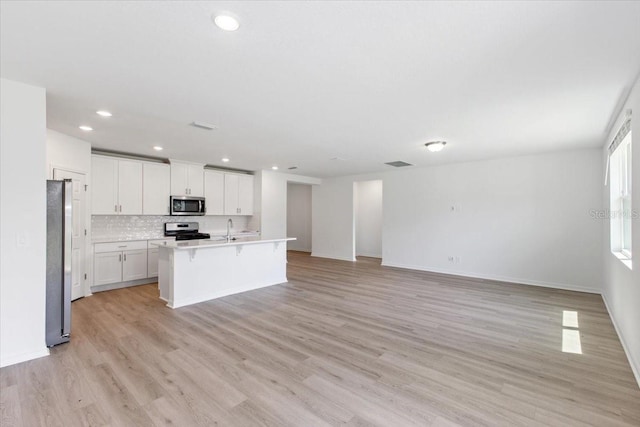 kitchen featuring stainless steel appliances, backsplash, an island with sink, white cabinets, and light wood-type flooring