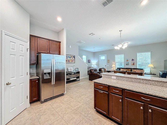 kitchen with dark brown cabinetry, stainless steel fridge, light stone countertops, and an inviting chandelier