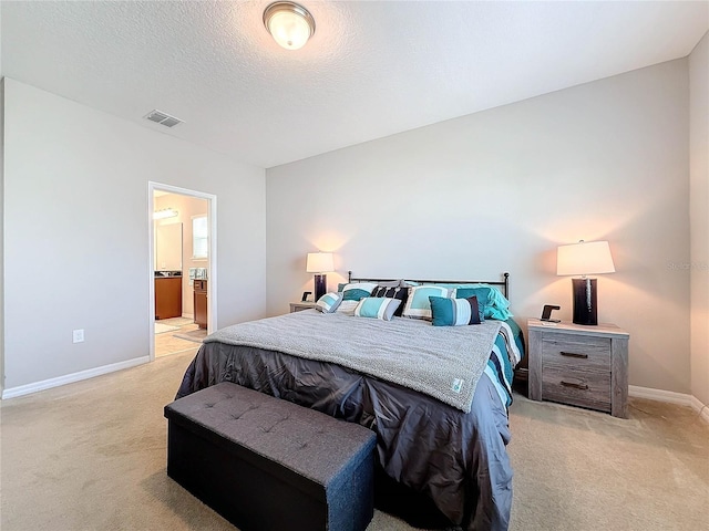 bedroom with ensuite bathroom, light carpet, and a textured ceiling