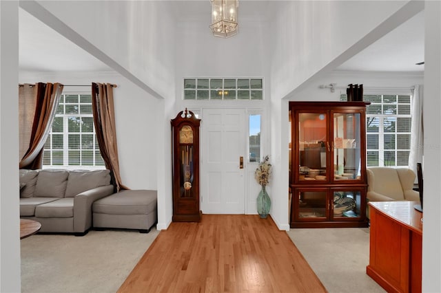 entryway with a chandelier, a towering ceiling, light wood-type flooring, and a healthy amount of sunlight