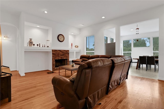 living room featuring a stone fireplace, a healthy amount of sunlight, and light hardwood / wood-style floors