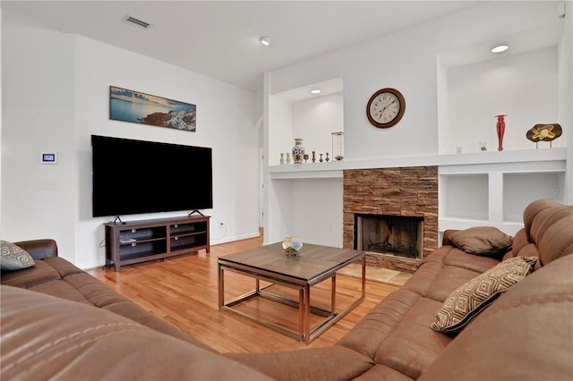 living room featuring hardwood / wood-style flooring, a stone fireplace, and built in features