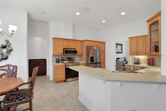 kitchen featuring kitchen peninsula, appliances with stainless steel finishes, tasteful backsplash, light tile patterned floors, and a breakfast bar area