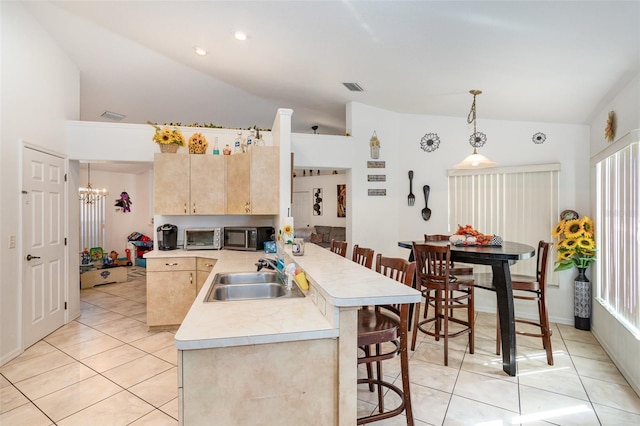 kitchen with sink, a kitchen breakfast bar, kitchen peninsula, vaulted ceiling, and decorative light fixtures