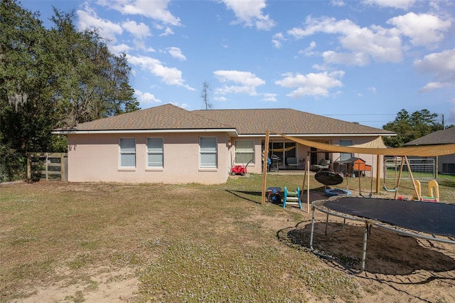 back of house featuring a playground, a trampoline, and a lawn