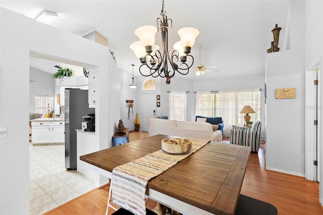 dining space featuring light hardwood / wood-style flooring, ceiling fan with notable chandelier, and vaulted ceiling