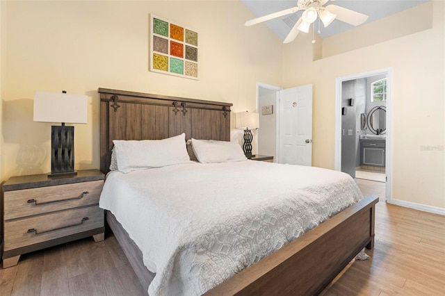 bedroom featuring ceiling fan, ensuite bathroom, light hardwood / wood-style floors, and a high ceiling