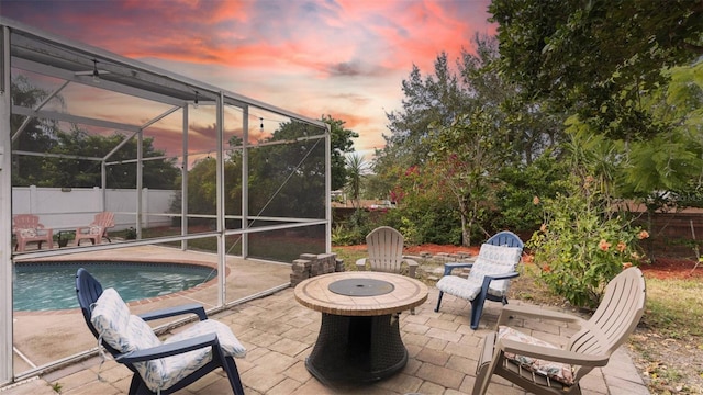 patio terrace at dusk with a lanai, a fenced in pool, and an outdoor fire pit