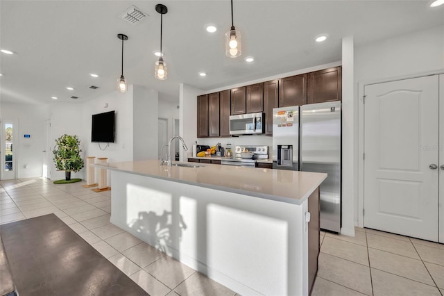 kitchen with a kitchen island with sink, hanging light fixtures, sink, dark brown cabinets, and stainless steel appliances