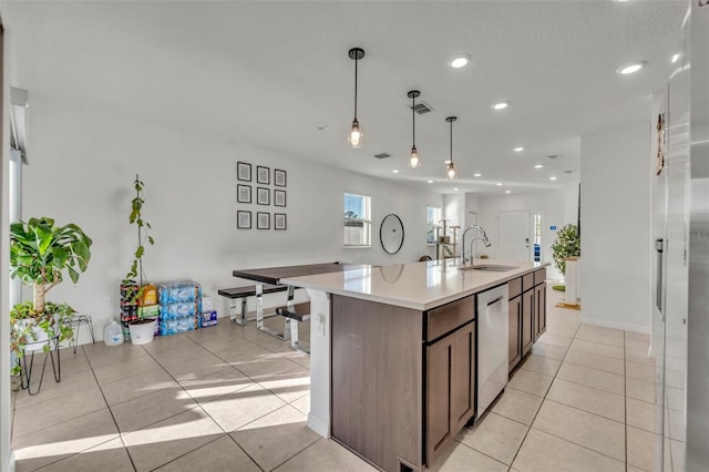 kitchen with dishwasher, a center island with sink, hanging light fixtures, dark brown cabinets, and light tile patterned flooring