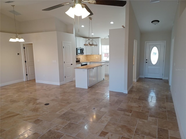 kitchen featuring appliances with stainless steel finishes, ceiling fan with notable chandelier, white cabinets, a center island, and butcher block countertops