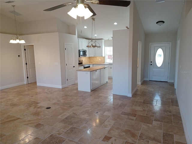 kitchen with baseboards, a kitchen island, stainless steel appliances, white cabinetry, and backsplash