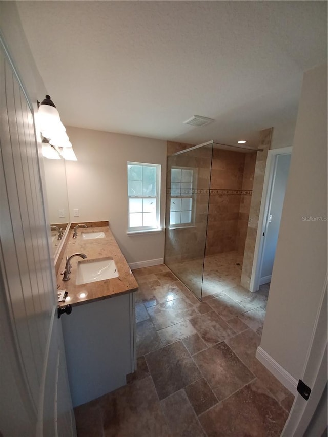 full bath featuring a sink, baseboards, walk in shower, and double vanity