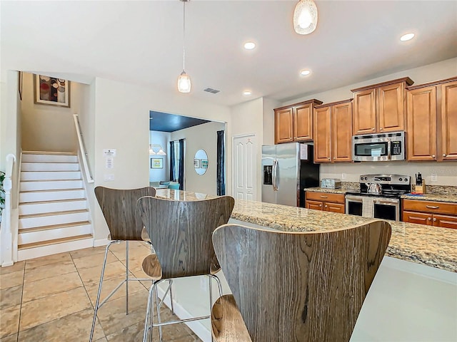 kitchen featuring light stone countertops, appliances with stainless steel finishes, a kitchen breakfast bar, decorative light fixtures, and light tile patterned flooring