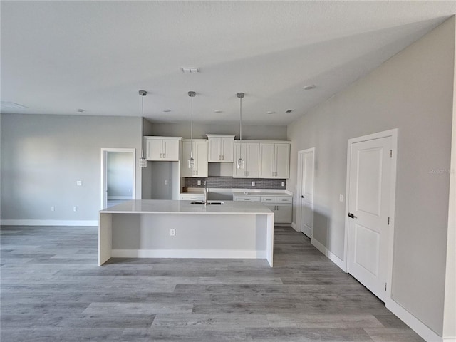 kitchen featuring sink, light hardwood / wood-style flooring, pendant lighting, a kitchen island with sink, and white cabinets