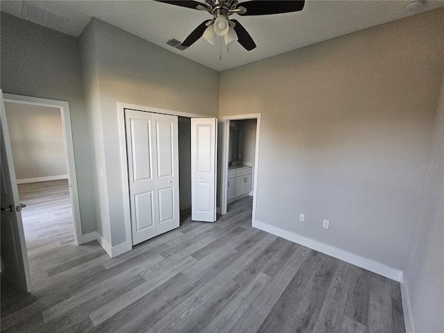 unfurnished bedroom with ceiling fan, a closet, light hardwood / wood-style floors, and a high ceiling